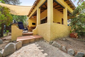 Ein überdachter Außenbereich mit Tisch und Stühlen, ein Steinweg, der zu einer Tür führt, und ein Blumentopf.