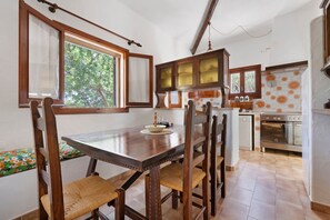 Eine Küche mit Holzausstattung, einem Esstisch, Stühlen und Blick ins Freie durch ein Fenster.