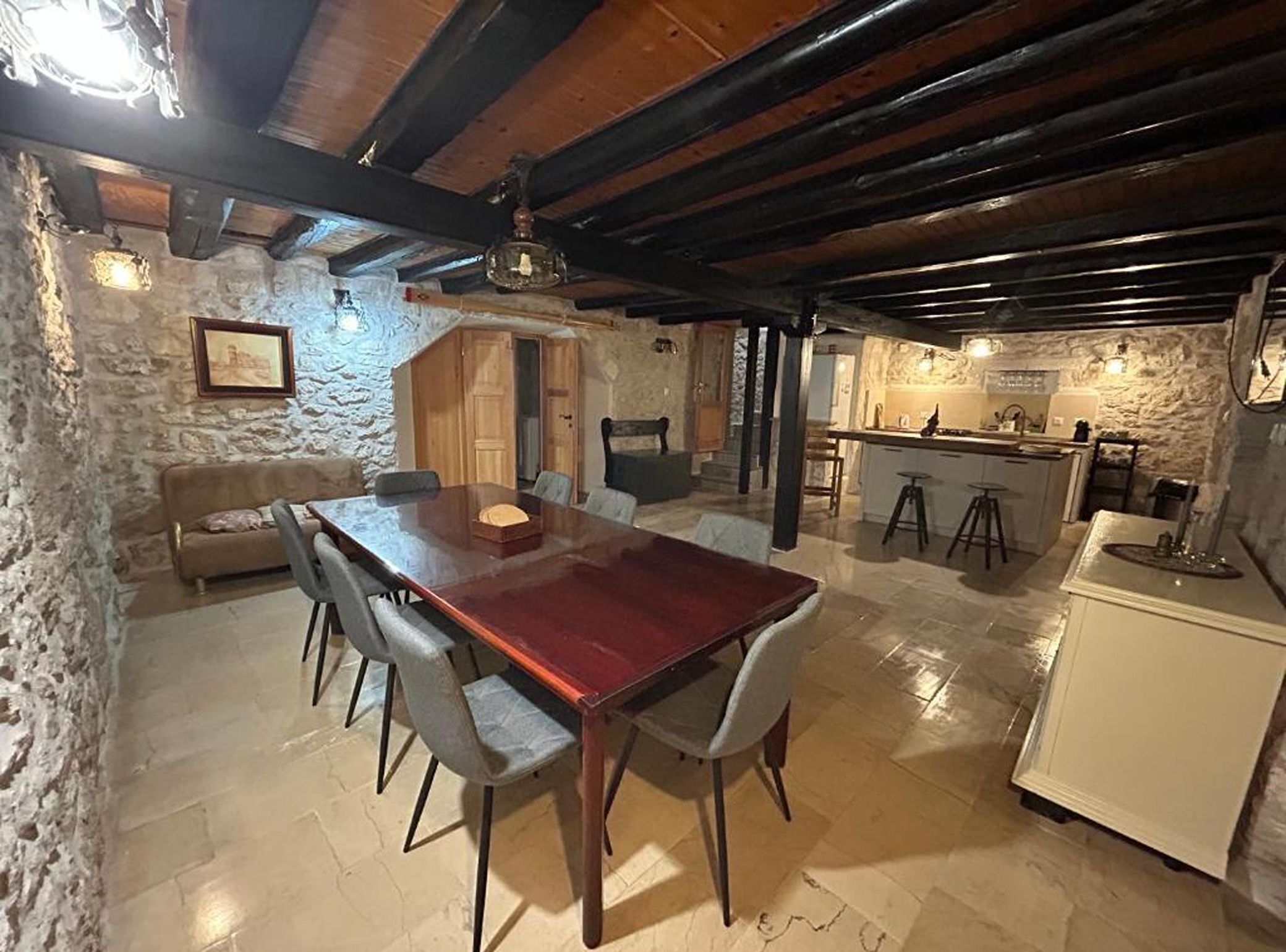 A rustic interior with a wooden dining table, chairs, a sofa, and a kitchen area.
