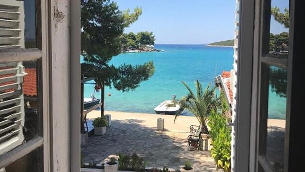 A view through a window of a coastal area with a beach, a boat, and a clear sky. - Lanterna Apartment With Hot-tub (Orebic)