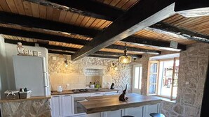 A kitchen with a stone wall, wooden beams, a large island, and two stools. - Lanterna Apartment With Hot-tub (Orebic)