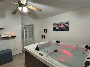 A spa room with a hot tub, ceiling fan, artwork, and a towel rack. - Lanterna Apartment With Hot-tub (Orebic)