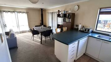 A compact kitchen with a dining area, a built-in bookshelf, and a large window.