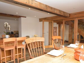 A dining area with wooden chairs and a table set for two, featuring a vase of flowers and a glass of wine. - 3 Bed in Exeter (oc-hobar) (Thorverton)