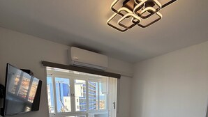 Un salon moderne avec un canapé gris, un téléviseur à écran plat fixé au mur et une table d’appoint en bois sur laquelle se trouve une télécommande.
