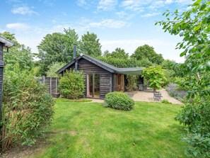 Une cabane en bois avec une porte en verre, entourée d’un jardin bien entretenu et d’un chemin de gravier.