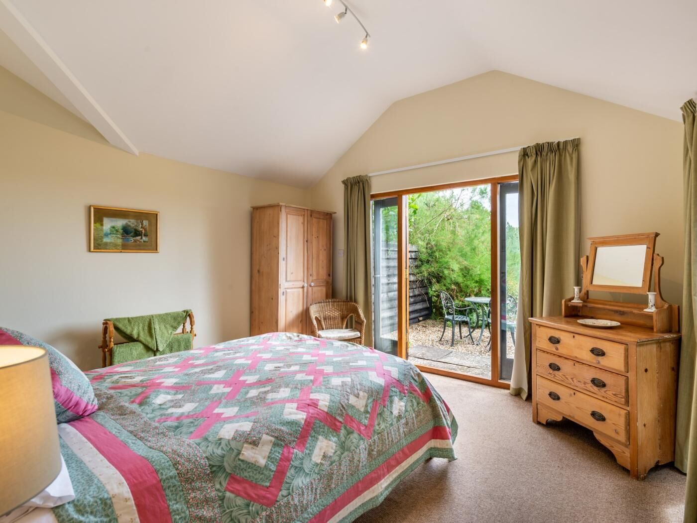 A bedroom with a bed, a wooden dresser, a chair, a table, and a sliding glass door leading to an outdoor area.