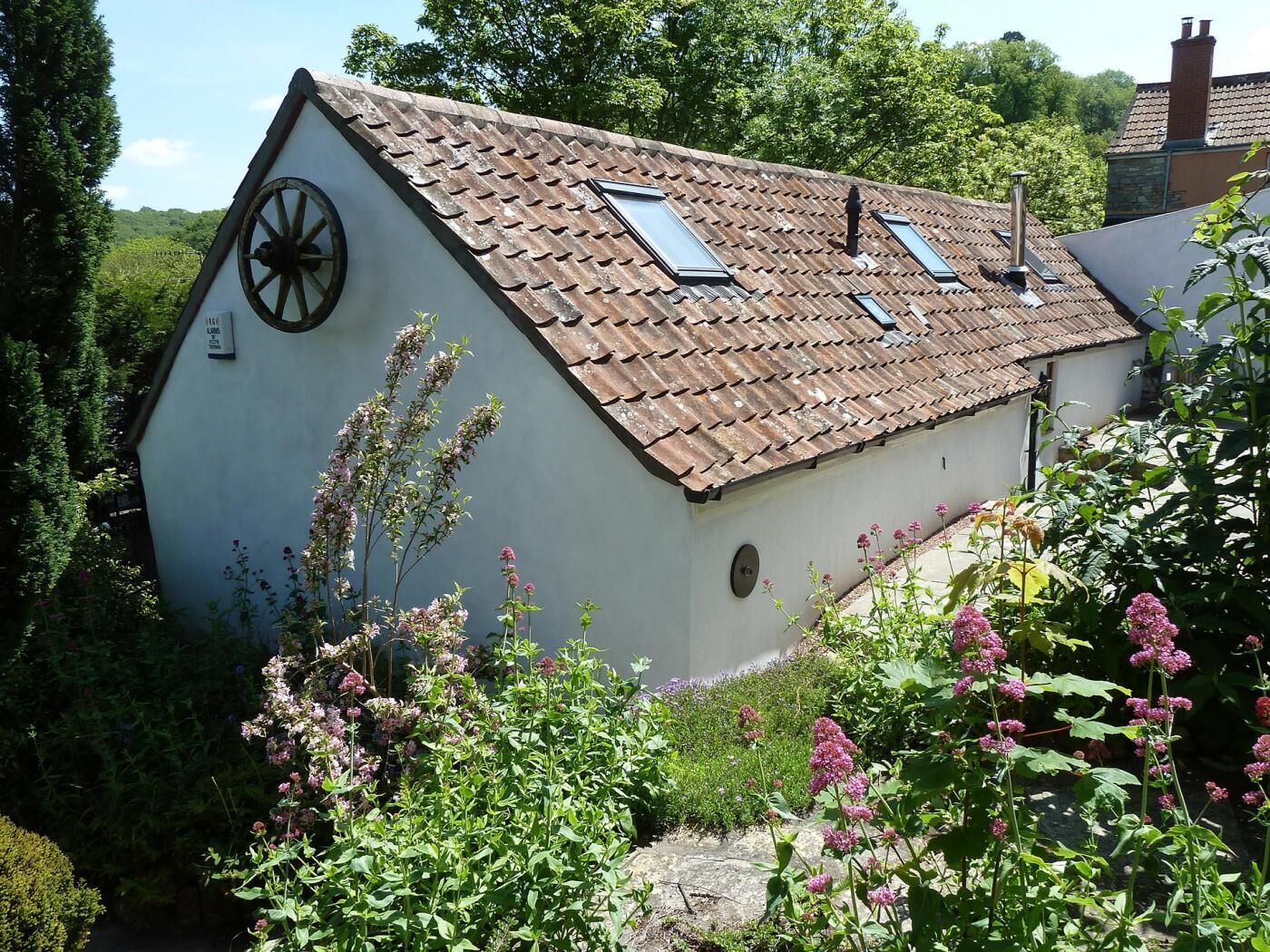 Un bâtiment blanc avec un toit en pente, un moulin à vent sur le côté et un jardin parsemé de fleurs roses.