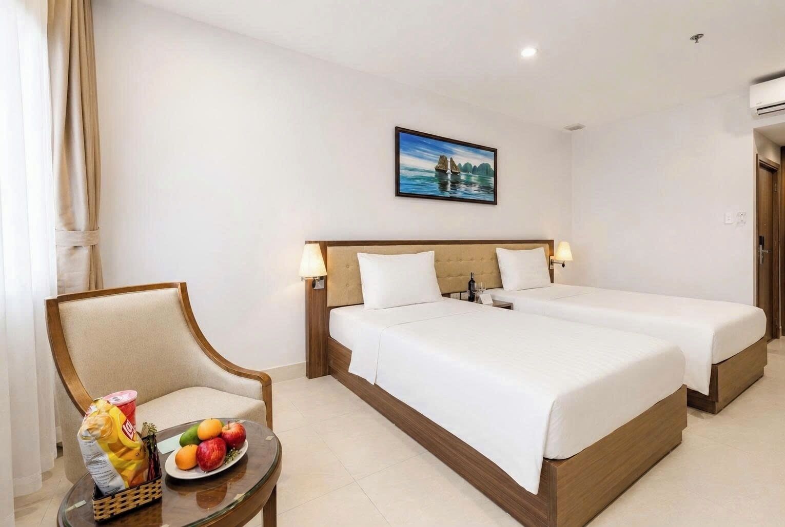 Habitación de hotel con dos camas, una silla, una mesa con fruta y un cuadro en la pared.