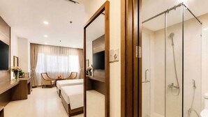 Quarto de hotel com cama, escrivaninha, televisão, chuveiro e espelho.
