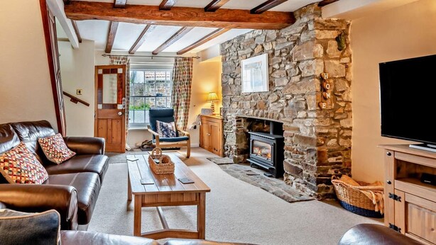 Ein gemütliches Wohnzimmer mit Kamin aus Stein, Ledersofas, einem Holztisch und einem Fernseher auf einem Holzständer.
