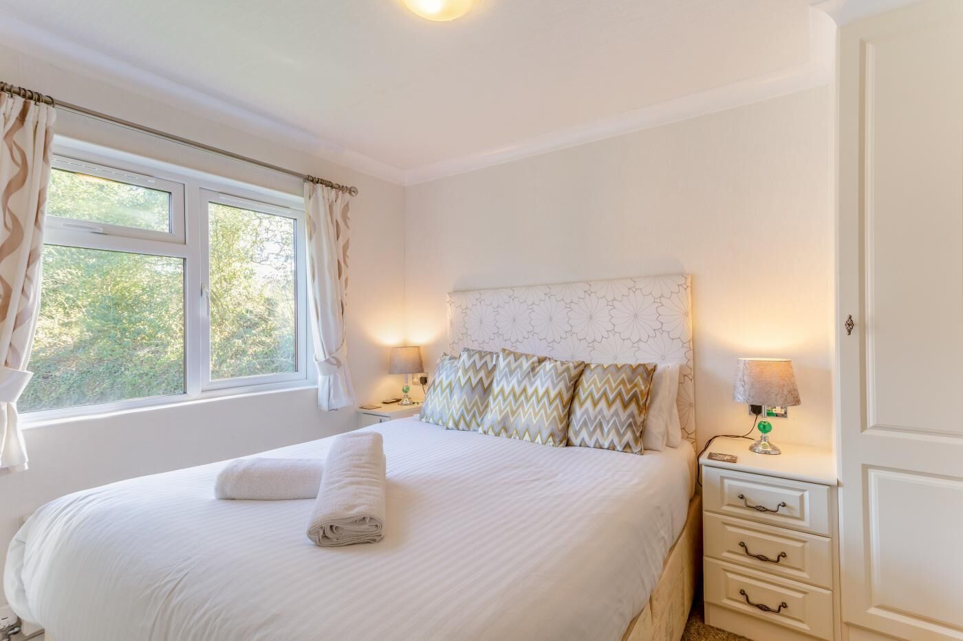 Une chambre à coucher avec un lit, deux tables de chevet, une commode, une fenêtre et une porte.