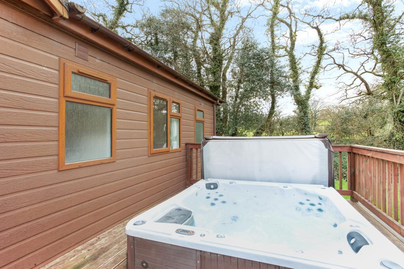 Una cabaña de madera con un jacuzzi en la terraza, rodeada de árboles.