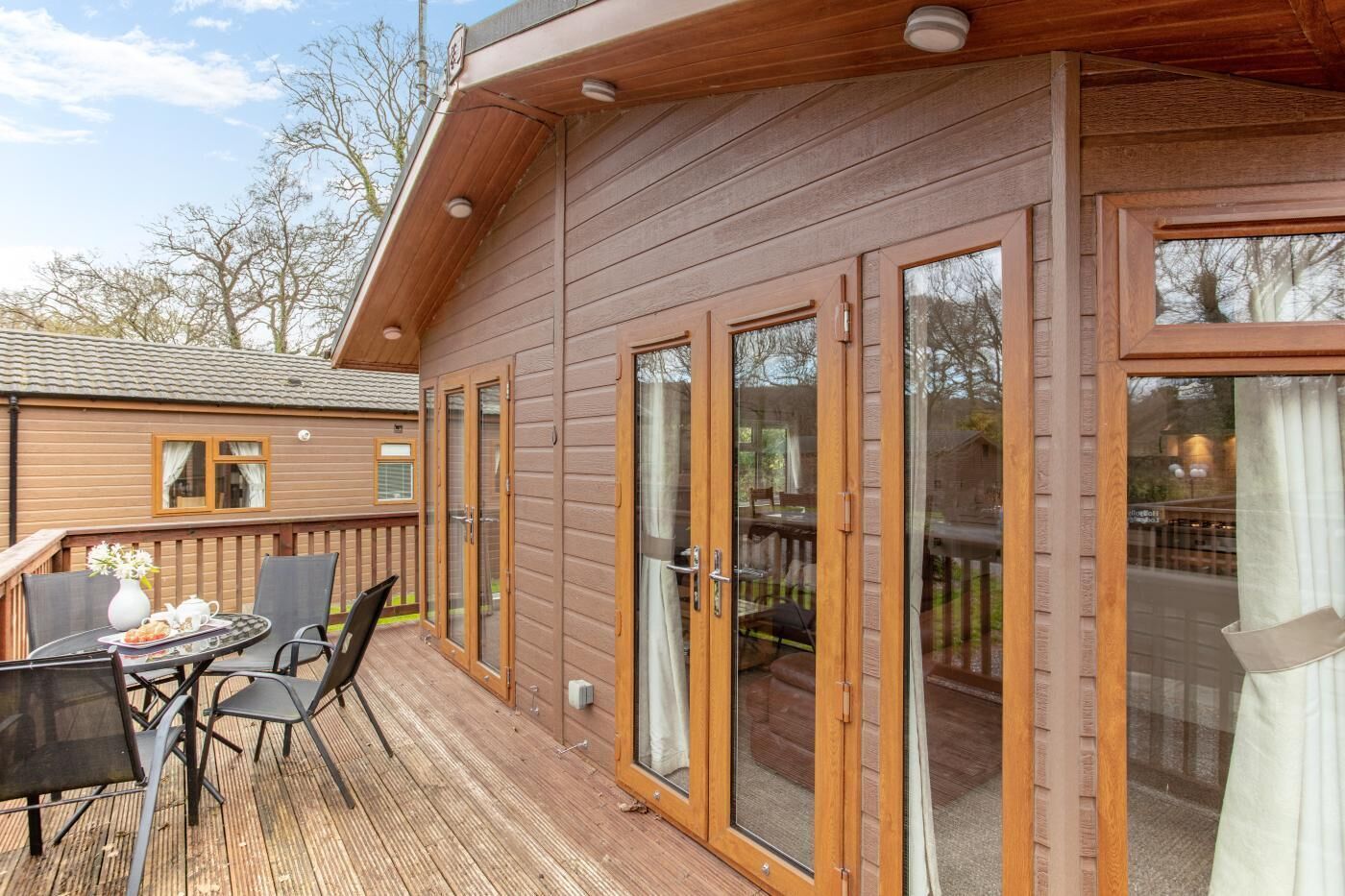 Une cabane en bois avec une terrasse, une table à manger avec des chaises et une grande porte-fenêtre coulissante.