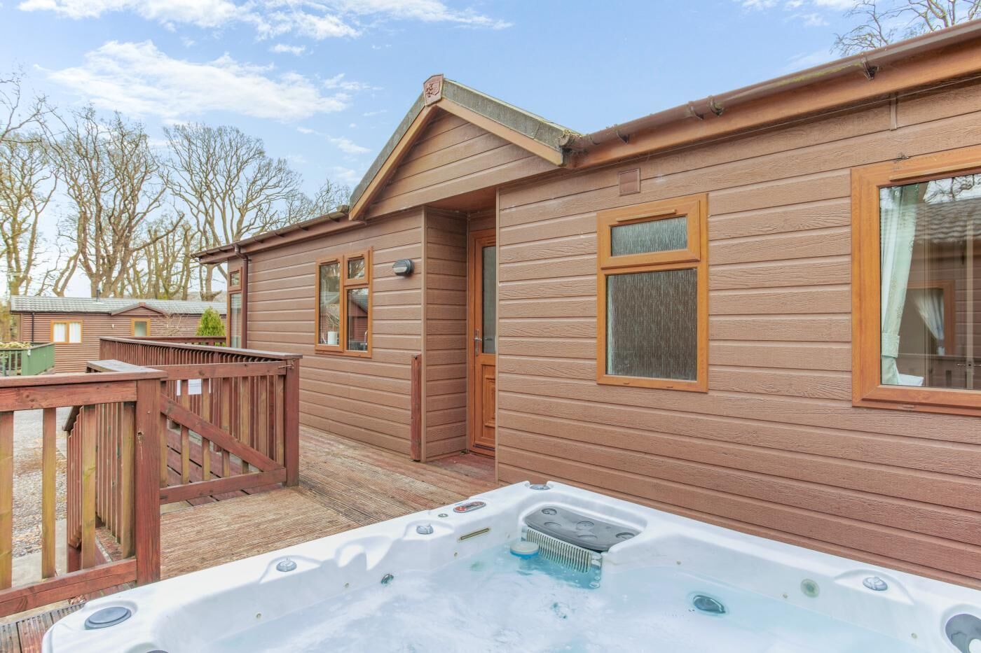 Una cabaña de madera con jacuzzi, terraza de madera y puerta de acceso al interior.