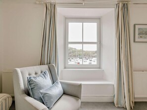 Ein Zimmer mit Fenster, einem Sessel mit Kissen und einem Heizkörper.