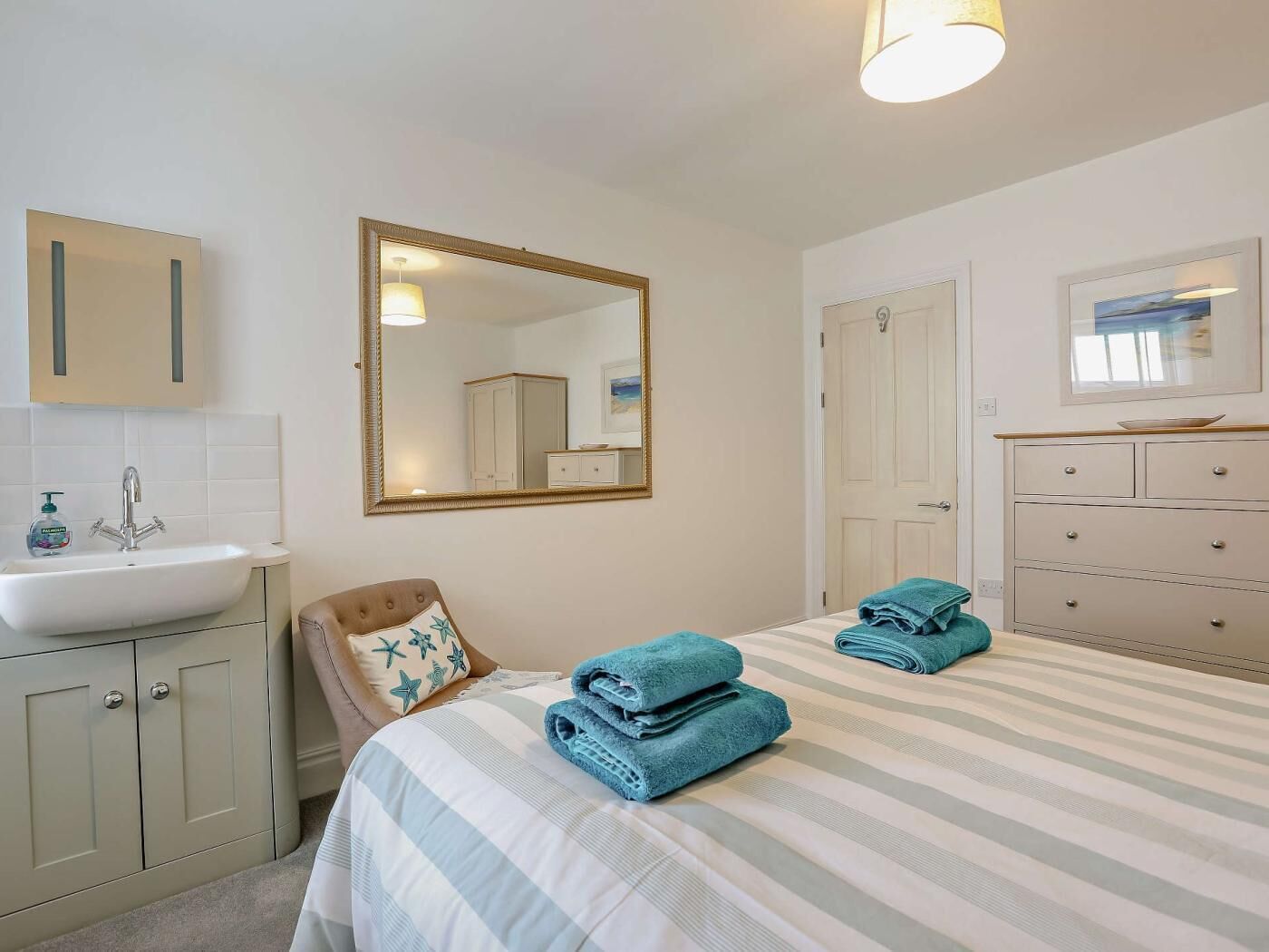 Een hotelkamer met een bed, een badkamer met wastafel en spiegel, een dressoir en een deur.