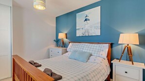 Une chambre à coucher comprenant un lit, deux tables de chevet, un banc en bois et une lampe fixée au mur.