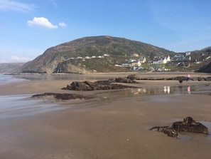 A coastal beach with a rocky shoreline, a hill with houses, and a person walking a dog. - 2 Bed in Haverfordwest (oc-50758) (Broad Haven)