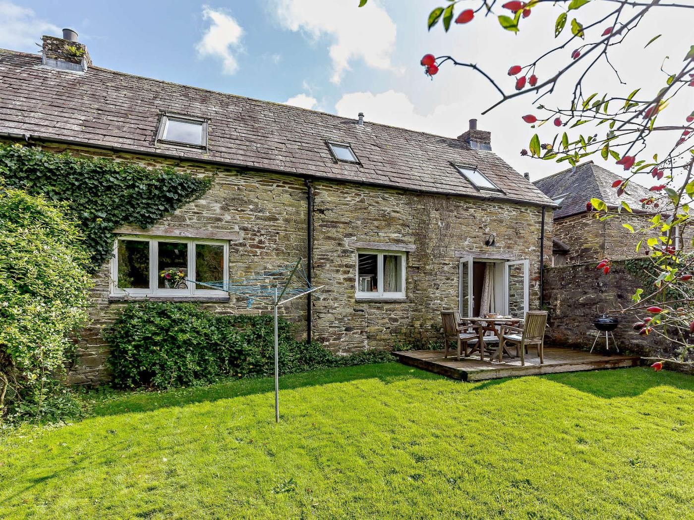 A stone house with a grassy yard, a patio with a table and chairs, and a chimney.