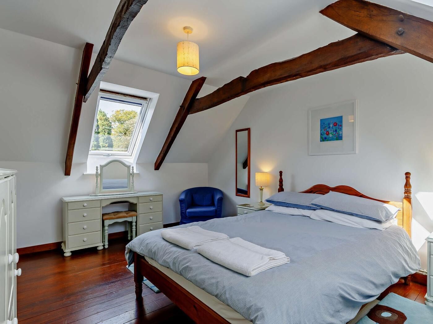 A bedroom with a bed, a desk, a chair, a window, and a painting on the wall.