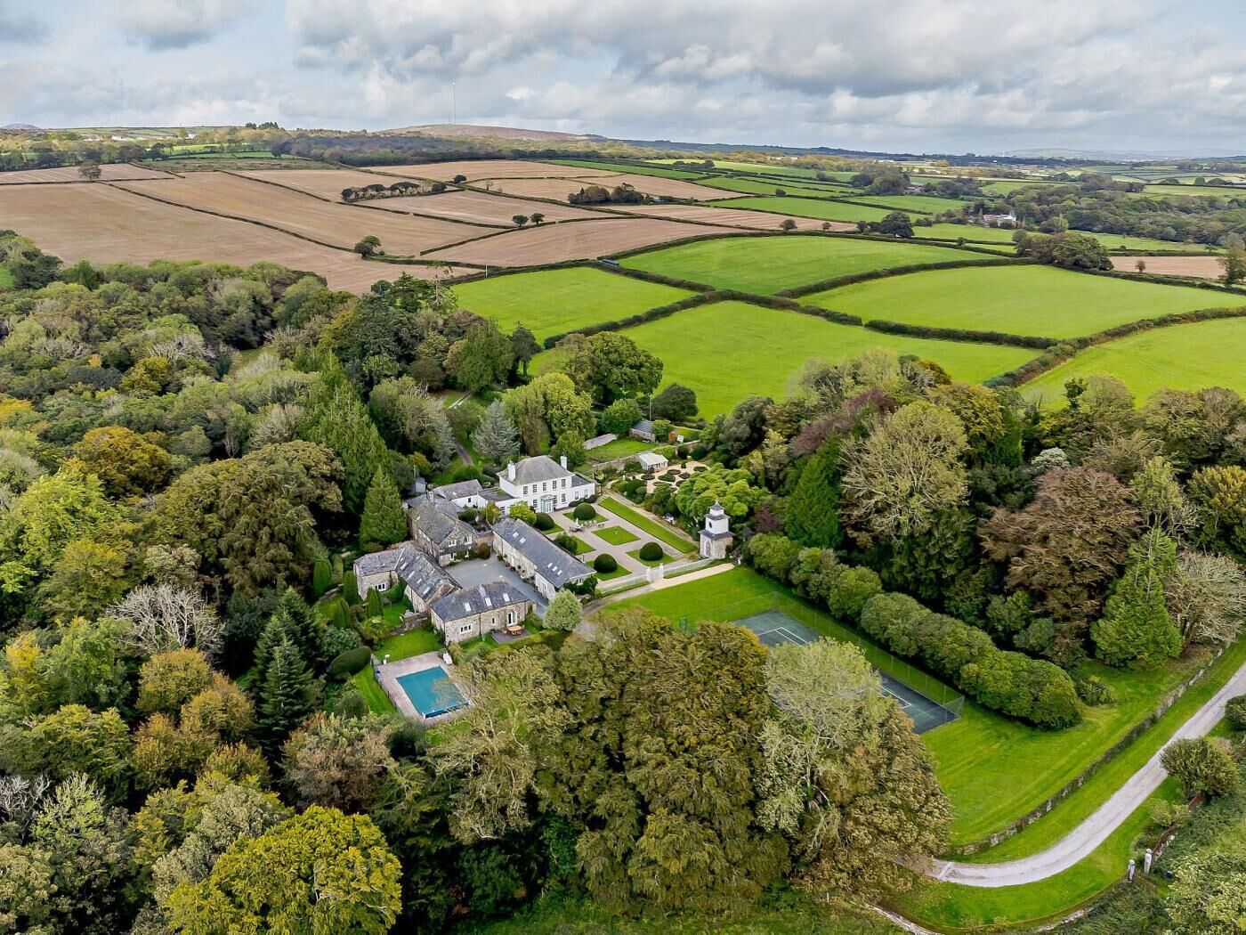 An aerial view of a large estate with expansive green fields, a swimming pool, and a formal garden.