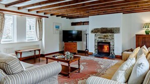 Ein Wohnzimmer mit freiliegenden Holzbalken, Kamin, Fernseher und einer Couch.