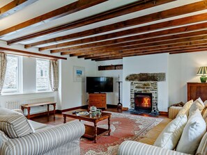 Ein Wohnzimmer mit freiliegenden Holzbalken, Kamin, Fernseher und einer Couch.