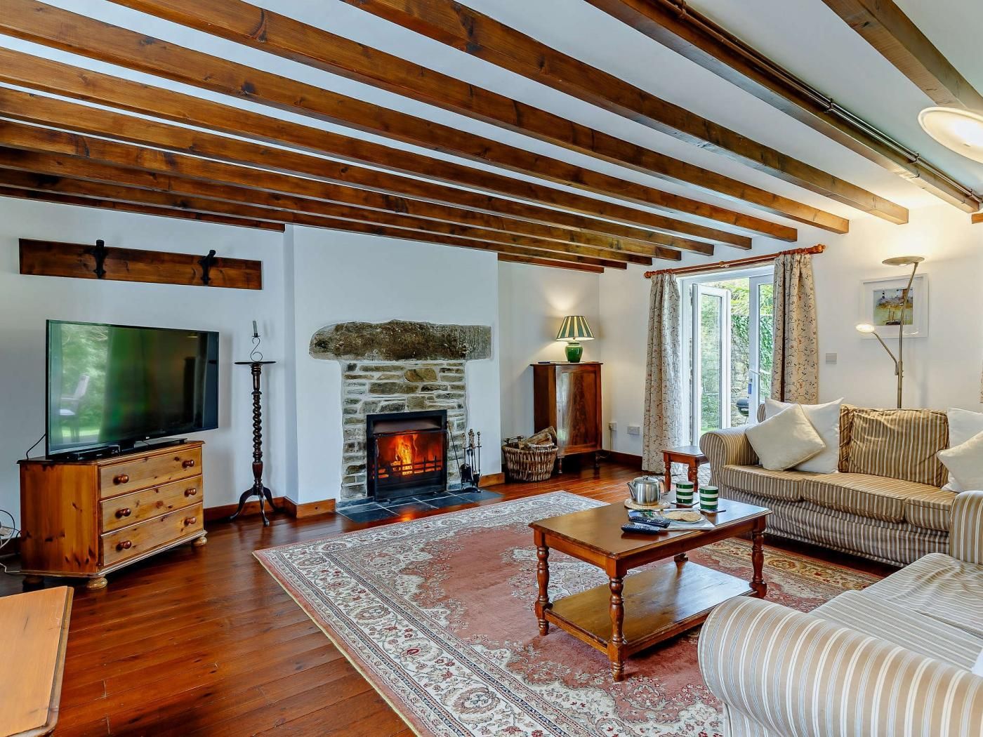 A living room with a stone fireplace, wooden beams, a television, a sofa, and a coffee table.