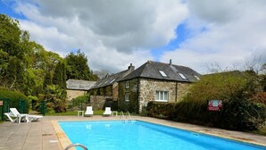 Ein Gebäude aus Stein mit einem Schwimmbecken, weißen Liegestühlen und einer Metalltreppe zum Pool.