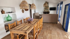 Uma área de refeições com mesa e cadeiras de madeira, um vaso verde, cestos de vime e uma lareira de pedra.