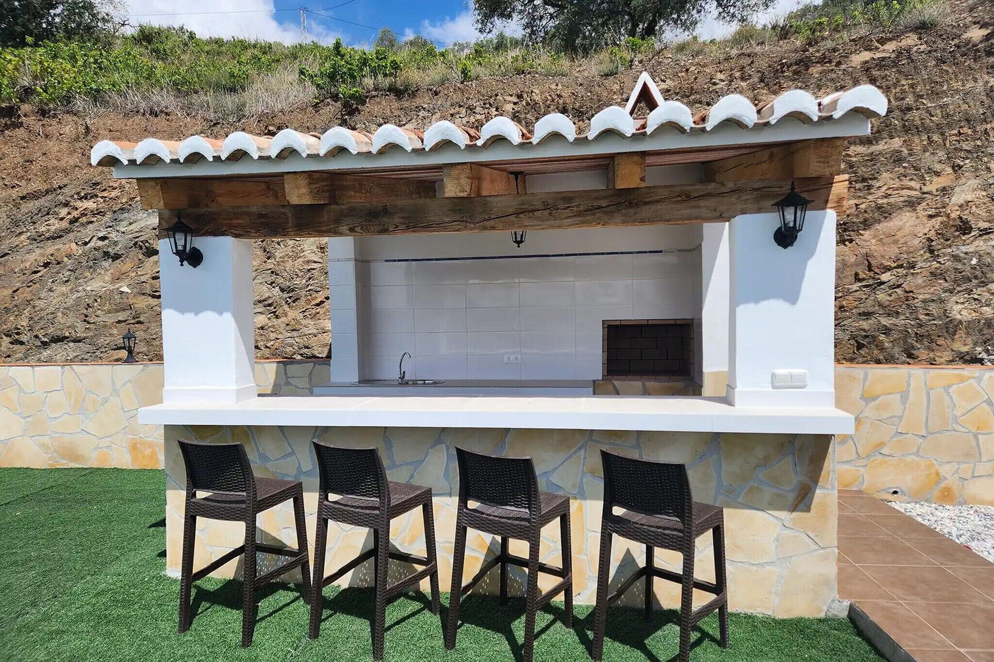 An outdoor bar with a stone wall, a tiled backsplash, and three wicker chairs.