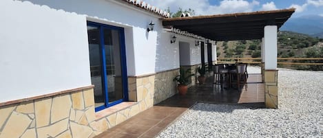 A building with a white exterior, a blue door, and a covered patio area with a table and chairs.