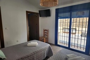 Ein Schlafzimmer mit einem Bett, einem Sessel, einem Fernseher und einem Fenster mit Blick auf einen Außenbereich.