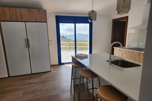 Une cuisine avec une grande fenêtre, un évier et deux tabourets.