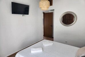 Une chambre d’hôtel avec un lit, un téléviseur fixé au mur, un miroir rond et une porte donnant sur une autre pièce.