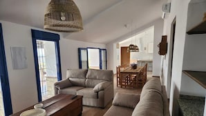 Uma sala de estar com sofá, mesa de centro de madeira e um espaço de jantar com mesa e cadeiras.