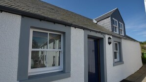 A white building with a dark blue door, a small window, and a visible light fixture. - 1 Bed in Kelso (oc-52538) (Morebattle)