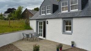 A two-story house with a grey roof, white exterior walls, and a patio with outdoor furniture. - 1 Bed in Kelso (oc-52538) (Morebattle)