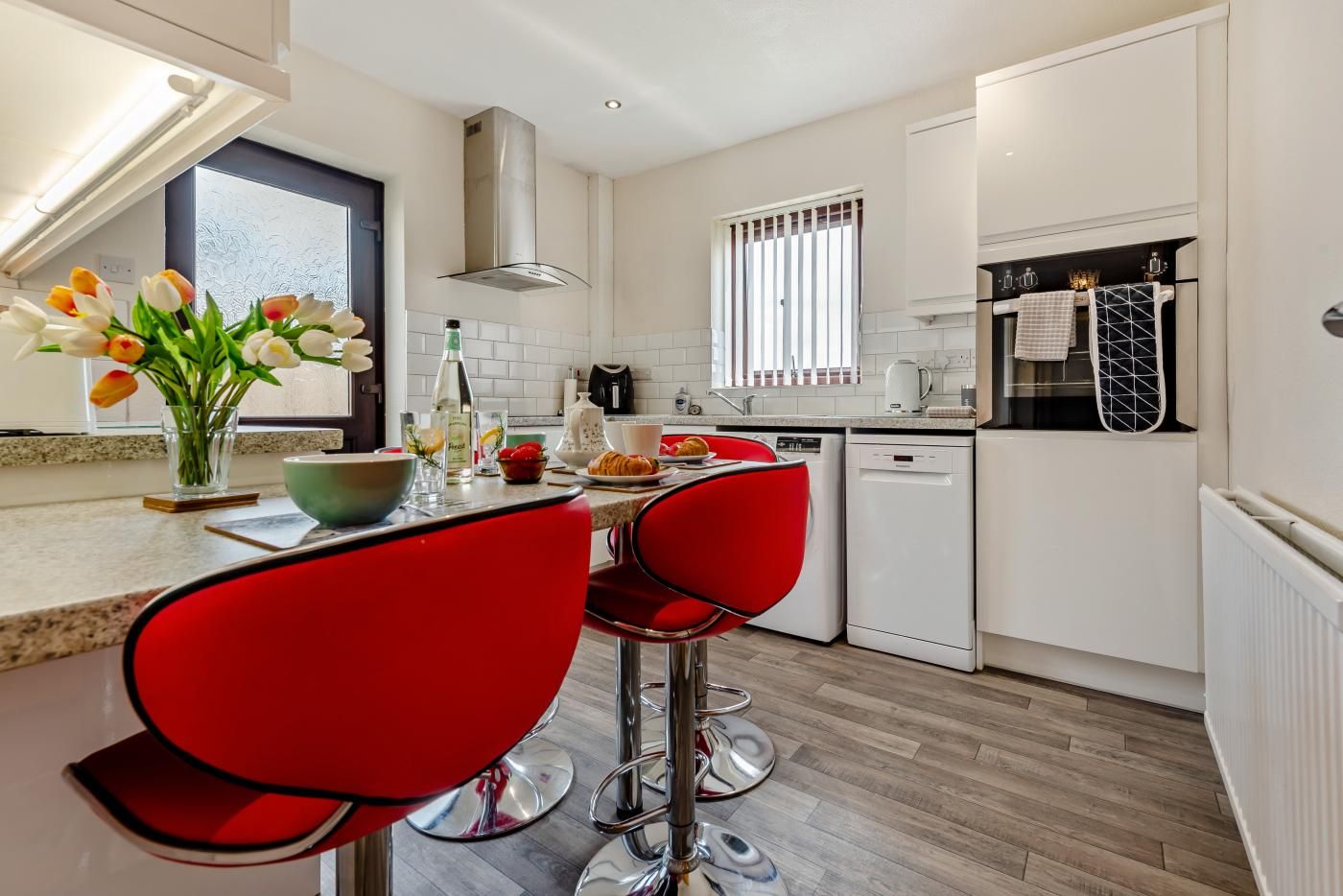 A modern kitchen with white cabinetry, a built-in oven, and a window with blinds.