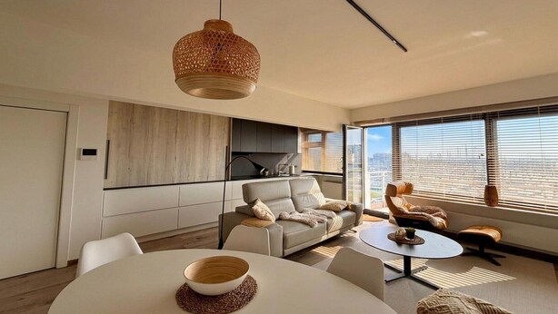 A modern living room with a sofa, a round table, and a hanging light fixture. - Charming Apartment Steps from Blankenberge Beach (Blankenberge)