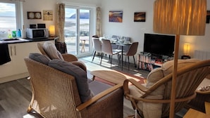 Ein modernes Wohnzimmer mit Essbereich, einem Fernseher und Blick auf den Strand.