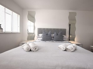 A neatly made bed with rolled towels, a grey headboard, and a large mirror on the wall. - 3 Bed in Ferryside (oc-53442) (Ferryside)