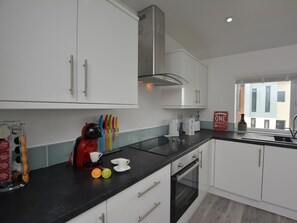 A modern kitchen with white cabinets, a black countertop, a coffee machine, and a window with a view of buildings. - 3 Bed in Ferryside (oc-53442) (Ferryside)