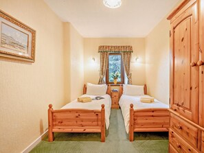 Een kamer met twee houten bedden, een groen vloerkleed, een houten kast en een lijst met een afbeelding aan de muur.