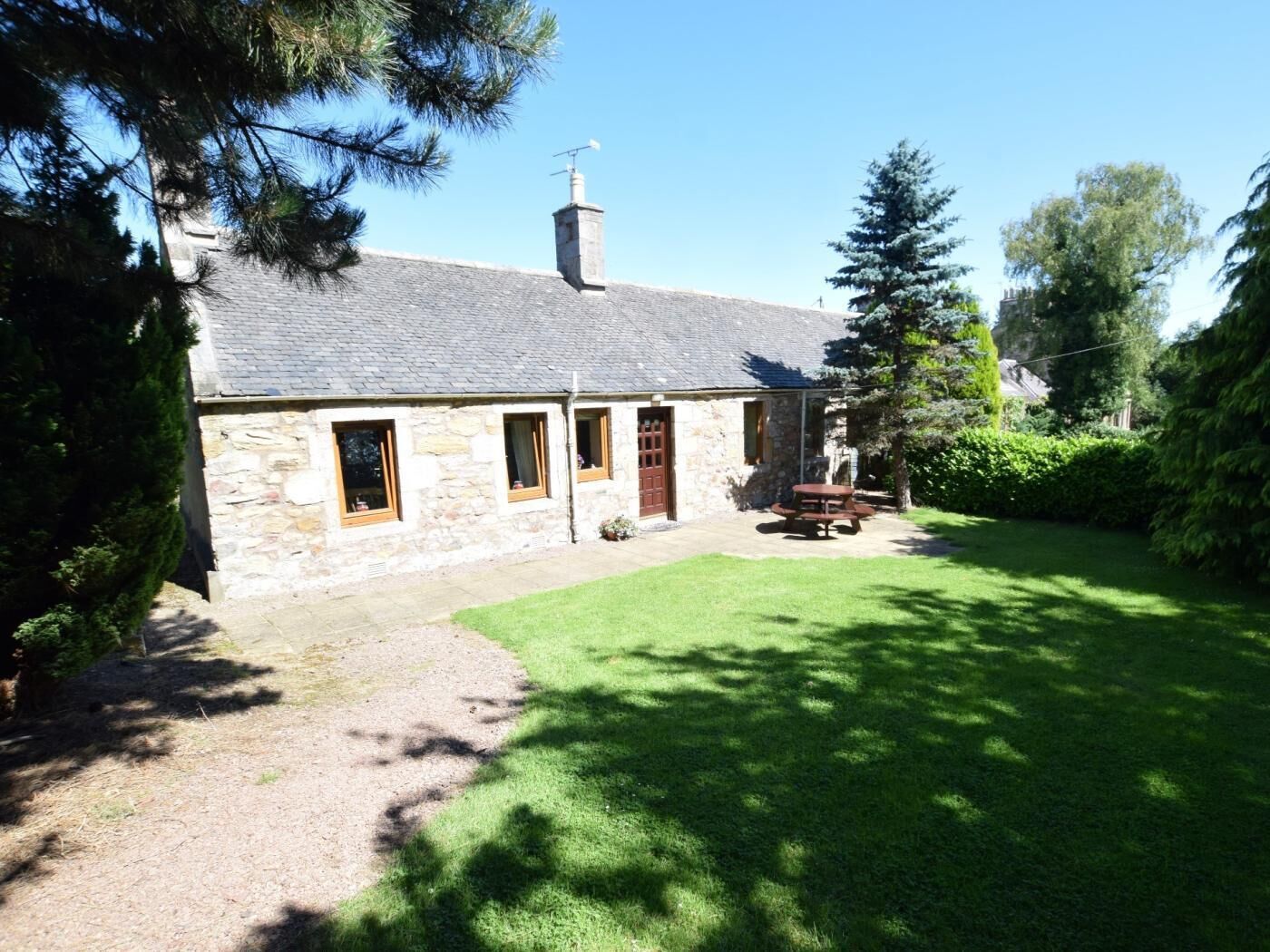 A stone cottage with a grassy yard, a wooden door, and a chimney.