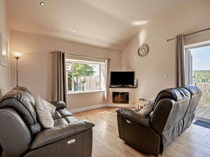 A modern living room with leather sofas, a flat-screen TV, and a fireplace. - 2 Bed in Blakeney (oc-54765) (Awre)