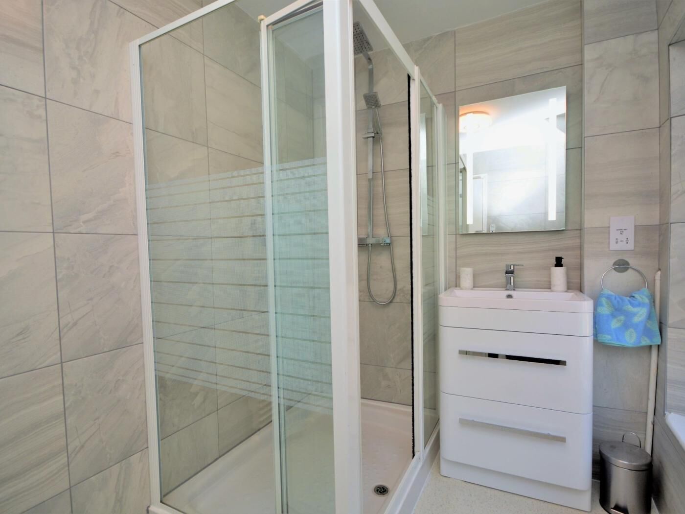 Un baño moderno con ducha de vidrio, tocador blanco con espejo y toallero.