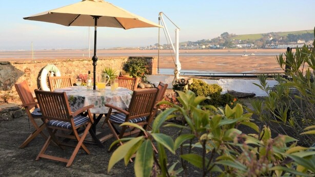 A table with chairs and an umbrella, overlooking a beach and distant buildings. - 3 Bed in Bideford (oc-55363) (Appledore)