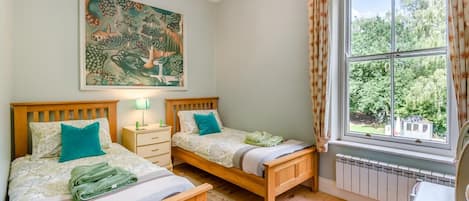 Un dormitorio con dos camas de madera, una mesita de noche, un cuadro y una ventana con vistas a zonas verdes.
